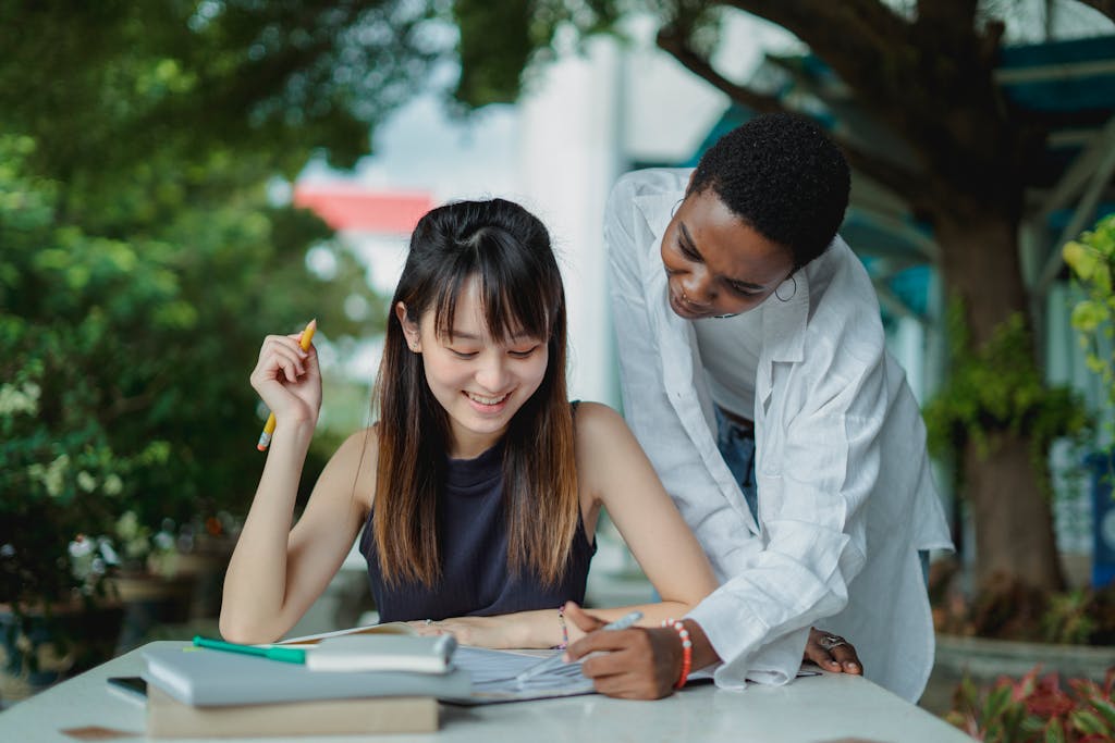 Young multiracial ladies spending time at table together while preparing for exam with books and wearing casual clothes in summer day outdoors